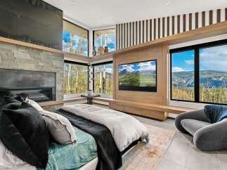 Experience luxury mountain living in this stunning bedroom featuring a modern stone fireplace and a large flat-screen TV.