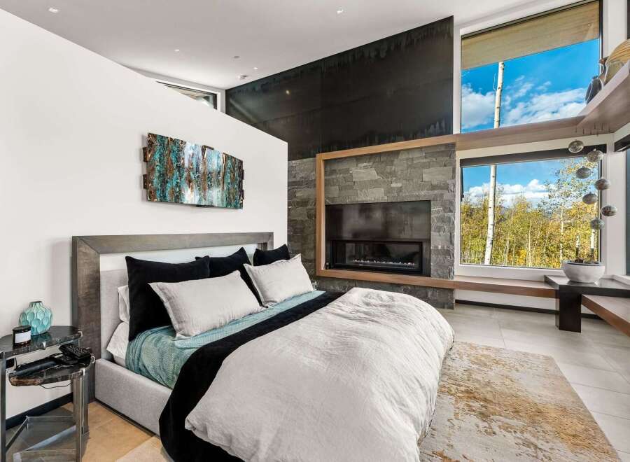 Experience luxury mountain living in this stunning bedroom featuring a modern gas fireplace with a stacked stone surround and a sleek black accent wall.