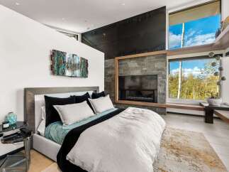 Experience luxury mountain living in this stunning bedroom featuring a modern gas fireplace with a stacked stone surround and a sleek black accent wall.