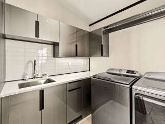 This modern laundry room features sleek, grey cabinetry with integrated handles, a white subway tile backsplash, and a stainless steel sink.