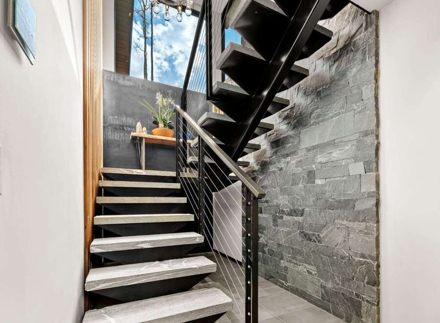 Experience modern living with this stunning staircase featuring sleek black metal treads and natural stone accents.