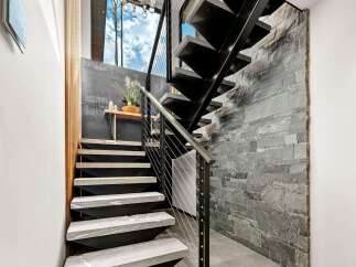 Experience modern living with this stunning staircase featuring sleek black metal treads and natural stone accents.