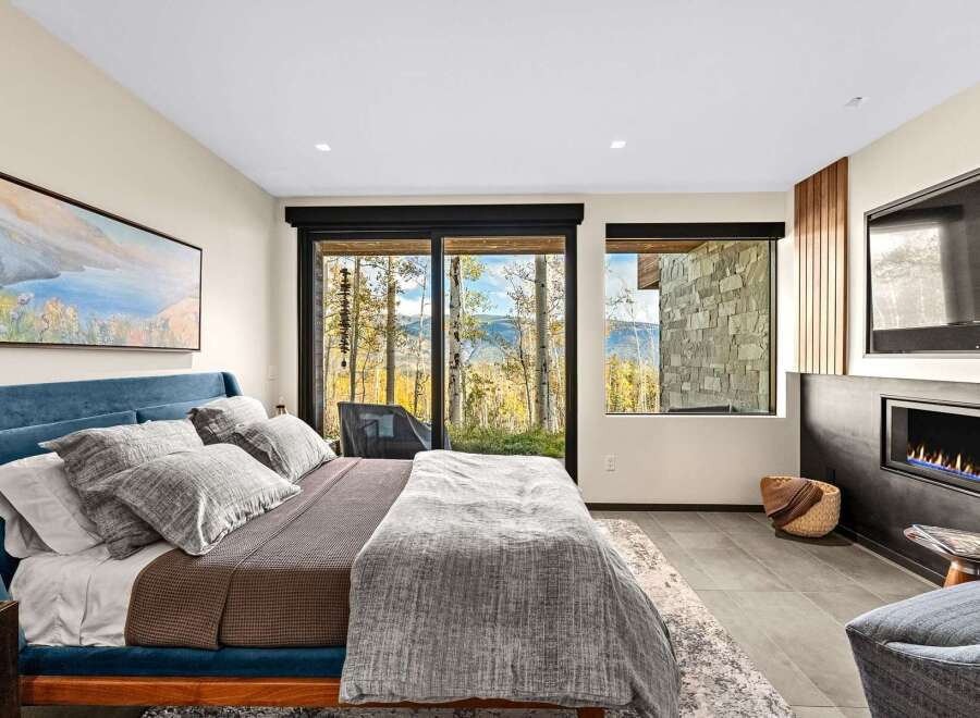 Experience luxury mountain living in this stunning bedroom featuring a plush blue velvet bed and a cozy fireplace.
