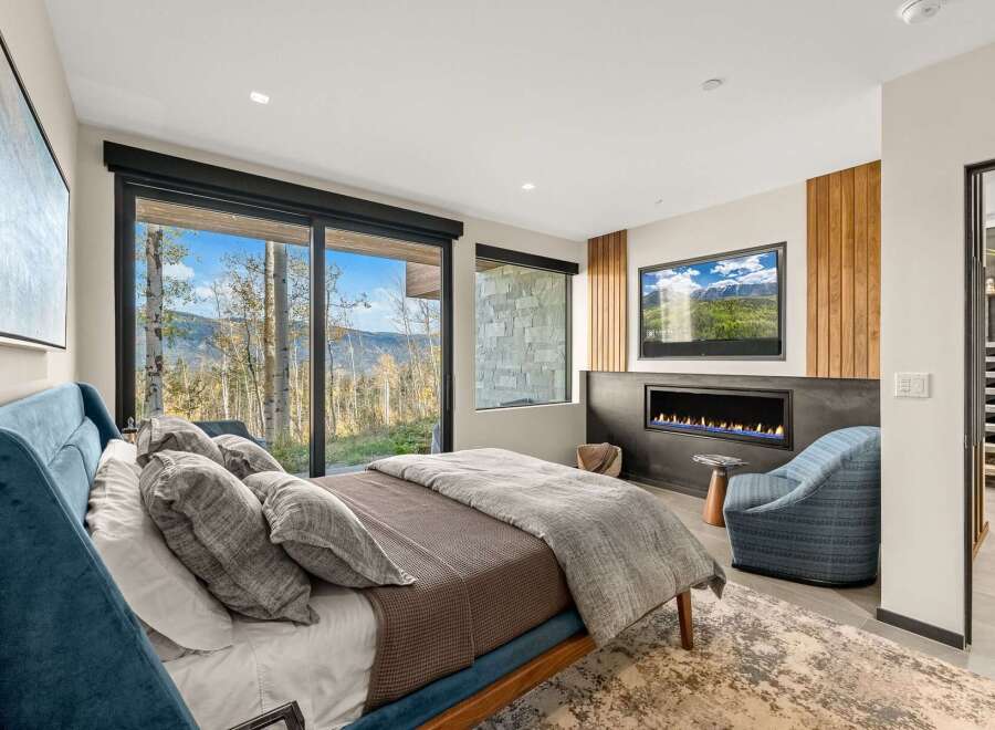 Experience luxury mountain living in this stunning bedroom featuring a modern gas fireplace and a large flat-screen TV.