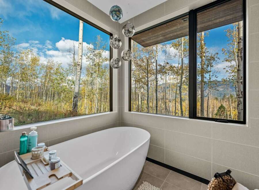 Experience ultimate relaxation in this luxurious bathroom, featuring a stunning freestanding bathtub with panoramic views of a vibrant autumn forest.