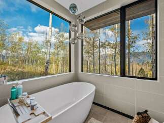 Experience ultimate relaxation in this luxurious bathroom, featuring a stunning freestanding bathtub with panoramic views of a vibrant autumn forest.