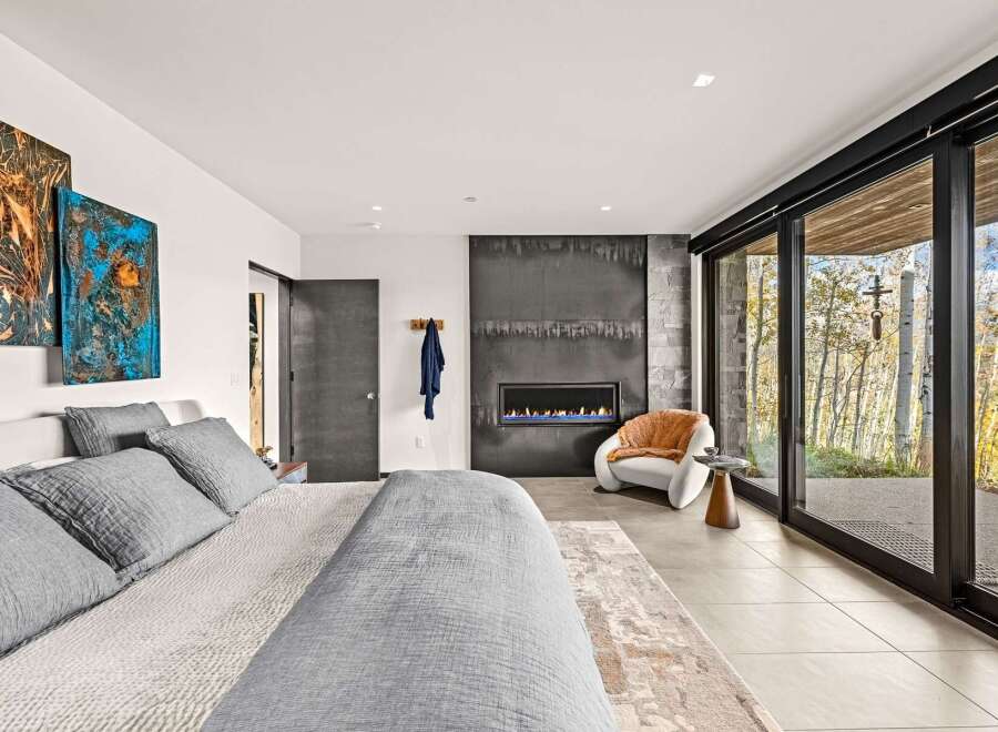 Experience modern luxury in this stunning bedroom featuring a sleek fireplace and expansive floor-to-ceiling windows that offer breathtaking views of the surrounding nature.