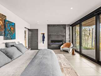 Experience modern luxury in this stunning bedroom featuring a sleek fireplace and expansive floor-to-ceiling windows that offer breathtaking views of the surrounding nature.