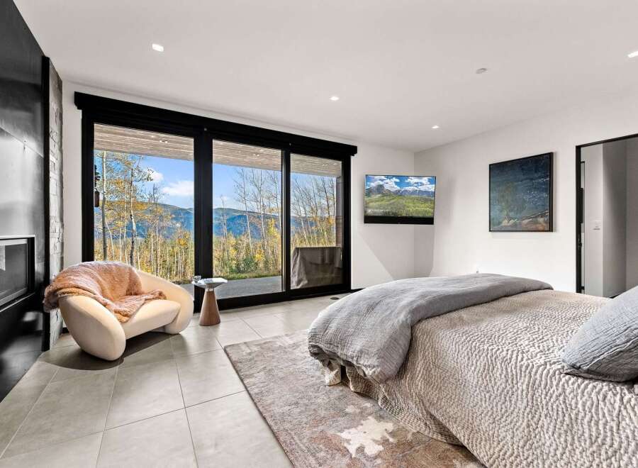 Experience breathtaking mountain views from this luxurious bedroom, featuring a cozy armchair and a modern fireplace.