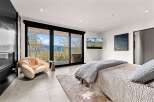 Experience breathtaking mountain views from this luxurious bedroom, featuring a cozy armchair and a modern fireplace.