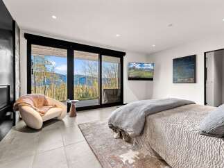 Experience breathtaking mountain views from this luxurious bedroom, featuring a cozy armchair and a modern fireplace.