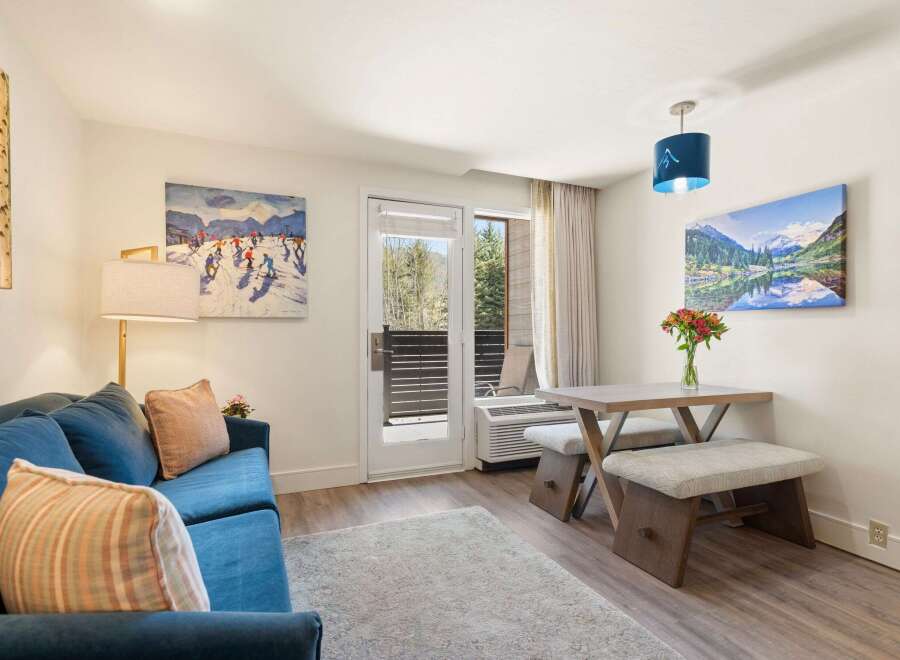 Experience mountain living in this charming studio, featuring a cozy blue sofa and a rustic dining area perfect for intimate meals.
