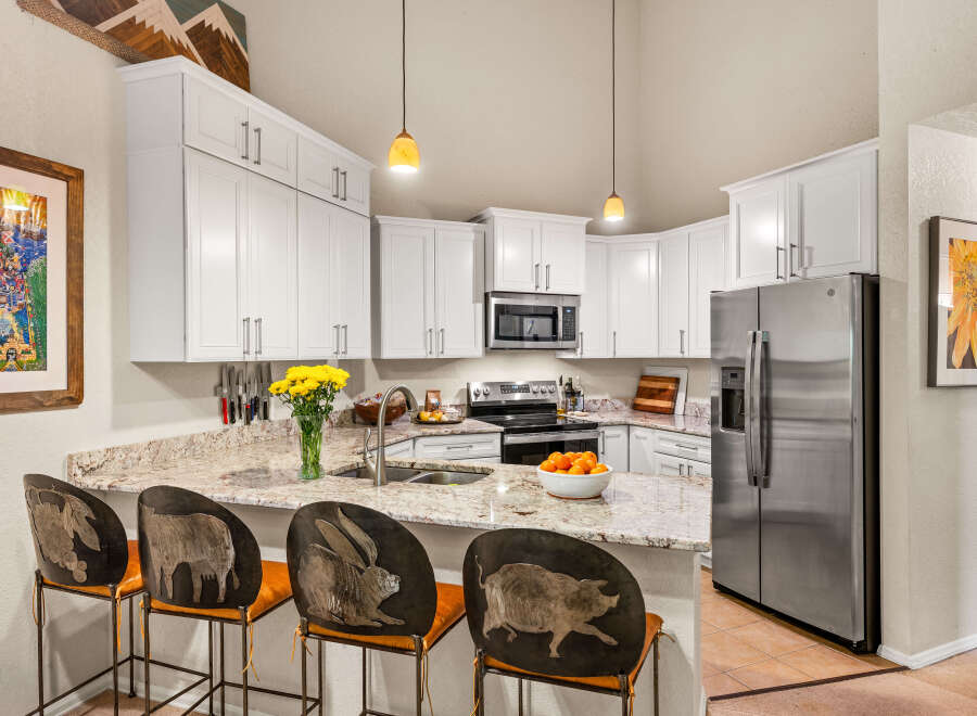 This stunning kitchen boasts pristine white cabinetry, granite countertops, and a large stainless steel refrigerator.