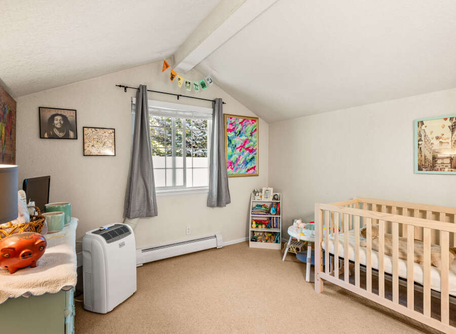 This charming nursery features a cozy crib, a white bookshelf filled with toys and books, and a colorful abstract painting.