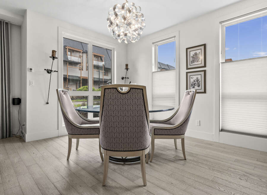 This dining area features a stylish chandelier and elegant upholstered chairs surrounding a glass-top dining table.