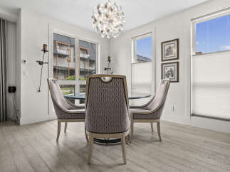 This dining area features a stylish chandelier and elegant upholstered chairs surrounding a glass-top dining table.