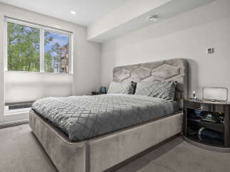 Experience modern comfort in this stylish bedroom, featuring a plush, upholstered bed with a unique geometric headboard and coordinating grey bedding.