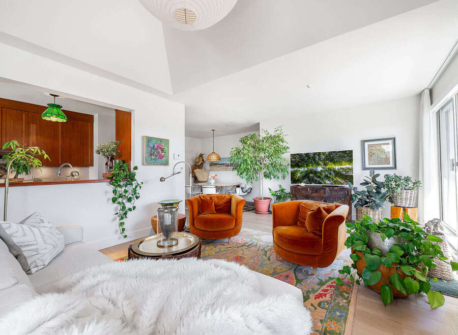 Experience modern living in this stylish living room, featuring plush orange velvet armchairs and a comfortable white sofa adorned with a faux fur throw.