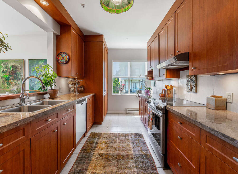 This spacious kitchen features warm cherry wood cabinetry, granite countertops, and a double stainless steel sink.