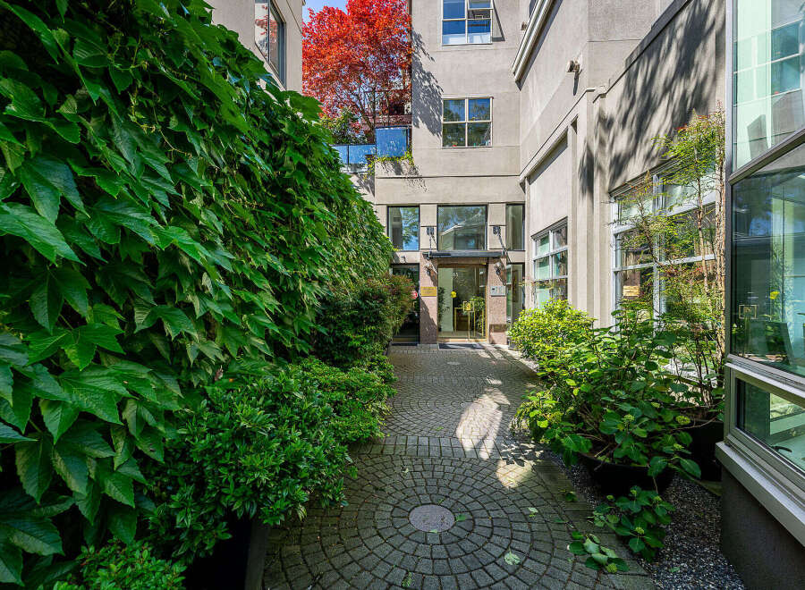 Discover the charm of this property's entrance, featuring a lush, ivy-covered wall on the left and a beautifully paved walkway leading to the building's entrance.
