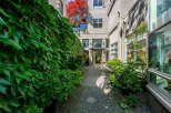 Discover the charm of this property's entrance, featuring a lush, ivy-covered wall on the left and a beautifully paved walkway leading to the building's entrance.