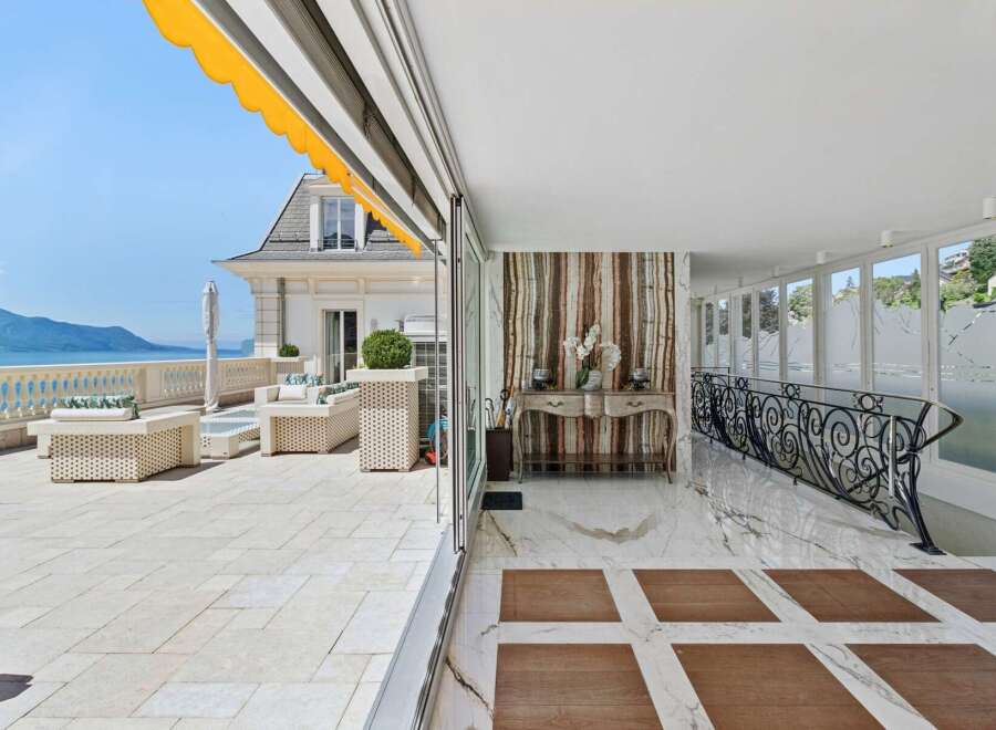 Experience luxurious outdoor living on this expansive terrace, featuring elegant wicker furniture and stunning lake and mountain views.