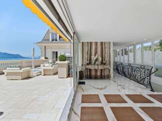 Experience luxurious outdoor living on this expansive terrace, featuring elegant wicker furniture and stunning lake and mountain views.