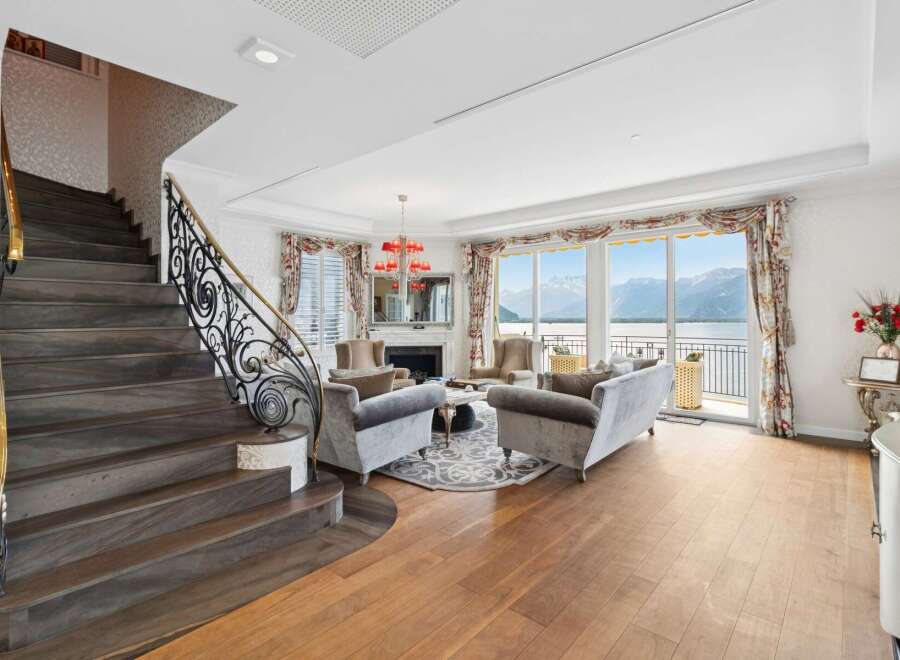 Experience luxurious living with this stunning living room featuring a grand staircase and elegant furnishings.