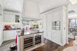Experience luxury in this stunning white kitchen, featuring a large central island with built-in wine coolers and a prominent range hood.