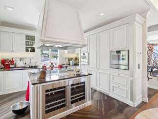 Experience luxury in this stunning white kitchen, featuring a large central island with built-in wine coolers and a prominent range hood.