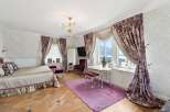 Experience opulent living in this luxurious bedroom featuring a grand bed with plush pillows and a ruffled skirt, complemented by rich, patterned curtains framing a stunning view.