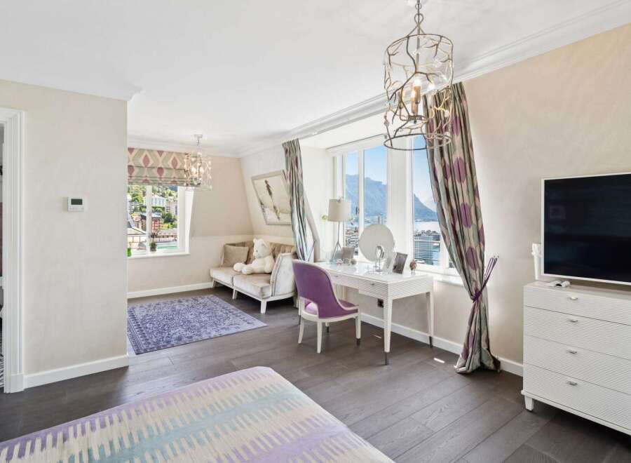 Experience luxury living in this beautifully appointed bedroom, featuring a charming vanity area with a purple chair and a stunning view of the lake and mountains.
