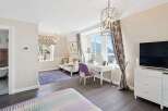 Experience luxury living in this beautifully appointed bedroom, featuring a charming vanity area with a purple chair and a stunning view of the lake and mountains.