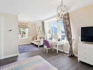 Experience luxury living in this beautifully appointed bedroom, featuring a charming vanity area with a purple chair and a stunning view of the lake and mountains.