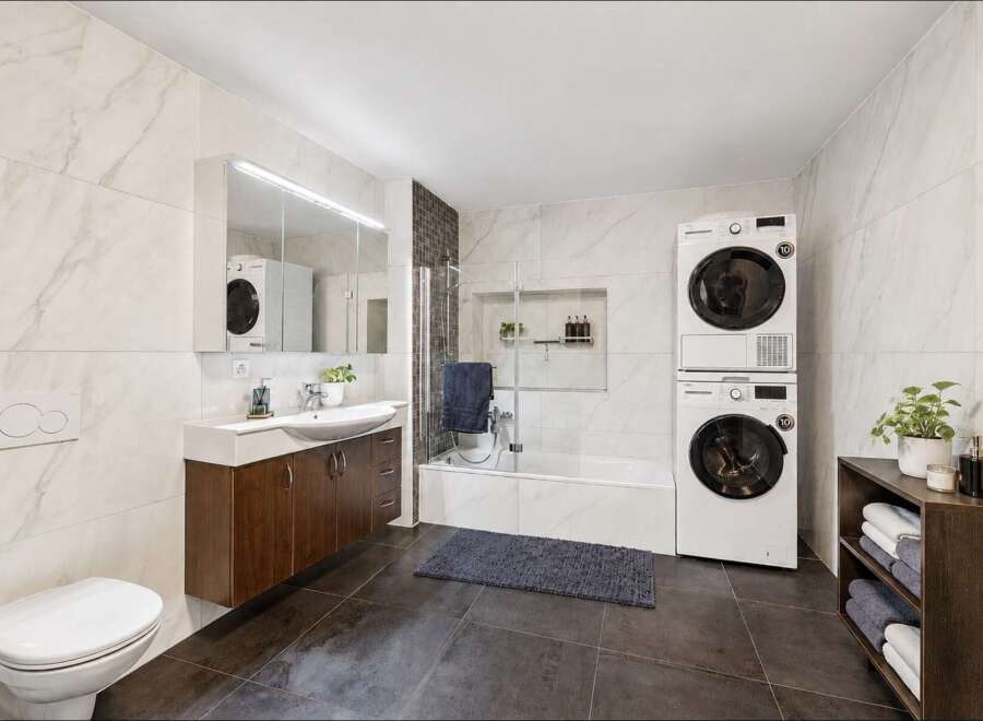 This modern bathroom features a sleek vanity with a vessel sink, a wall-mounted toilet, and a bathtub with a glass shower enclosure.