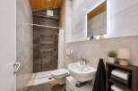 This modern bathroom features a spacious walk-in shower with dark tiled walls, complemented by a sleek white toilet and a stylish vanity with a vessel sink.