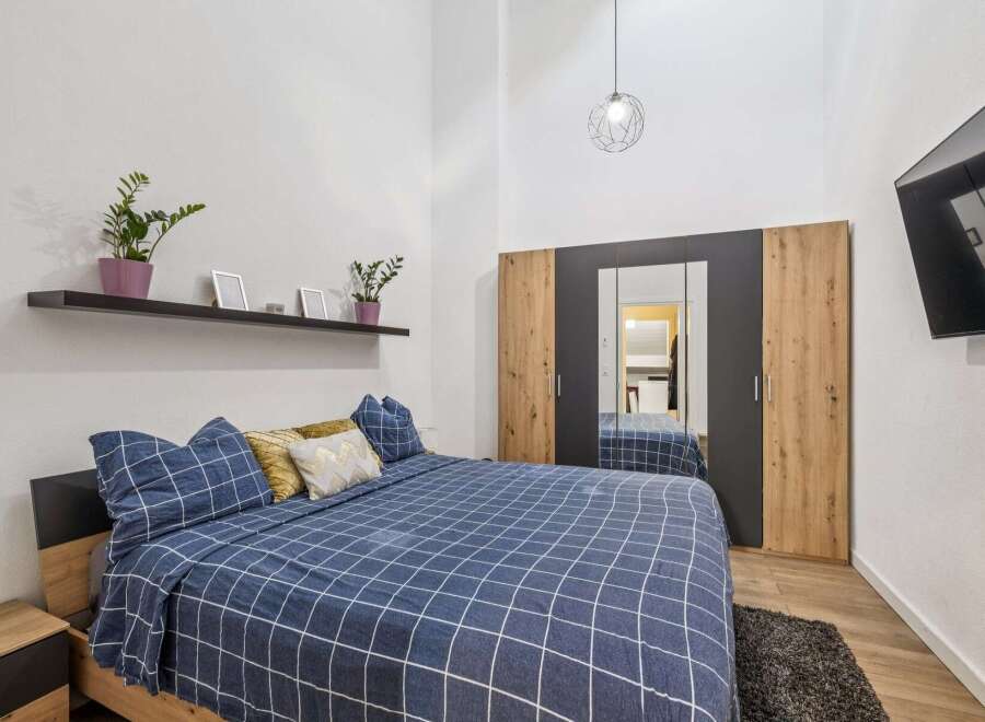 Experience modern comfort in this stylish bedroom, featuring a spacious bed with a blue checkered duvet and plush pillows.