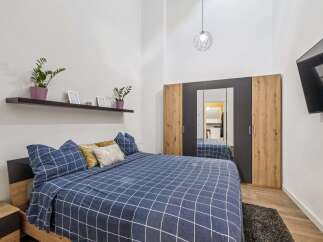 Experience modern comfort in this stylish bedroom, featuring a spacious bed with a blue checkered duvet and plush pillows.