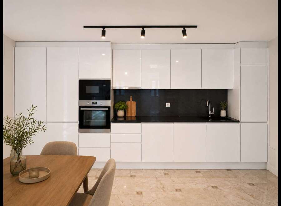 Experience modern living in this sleek kitchen featuring high-gloss white cabinetry and integrated stainless steel appliances, including a microwave and oven.