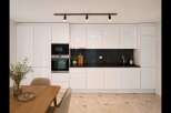 Experience modern living in this sleek kitchen featuring high-gloss white cabinetry and integrated stainless steel appliances, including a microwave and oven.