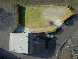 Discover this aerial view showcasing a property with a spacious paved parking area and a well-maintained lawn, perfect for outdoor activities.
