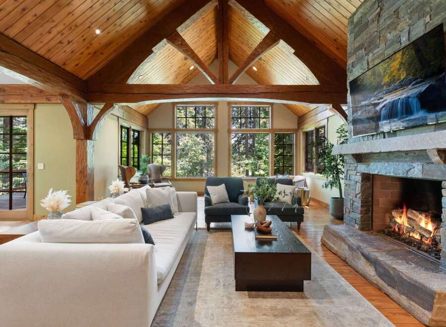 Experience rustic luxury in this stunning living room, featuring a soaring vaulted ceiling with exposed wooden beams and a grand stone fireplace.