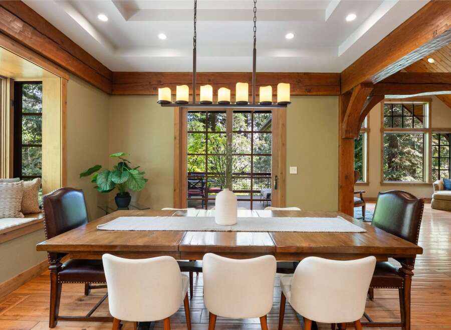 Experience rustic elegance in this spacious dining room, featuring exposed wooden beams and a large window overlooking lush greenery.