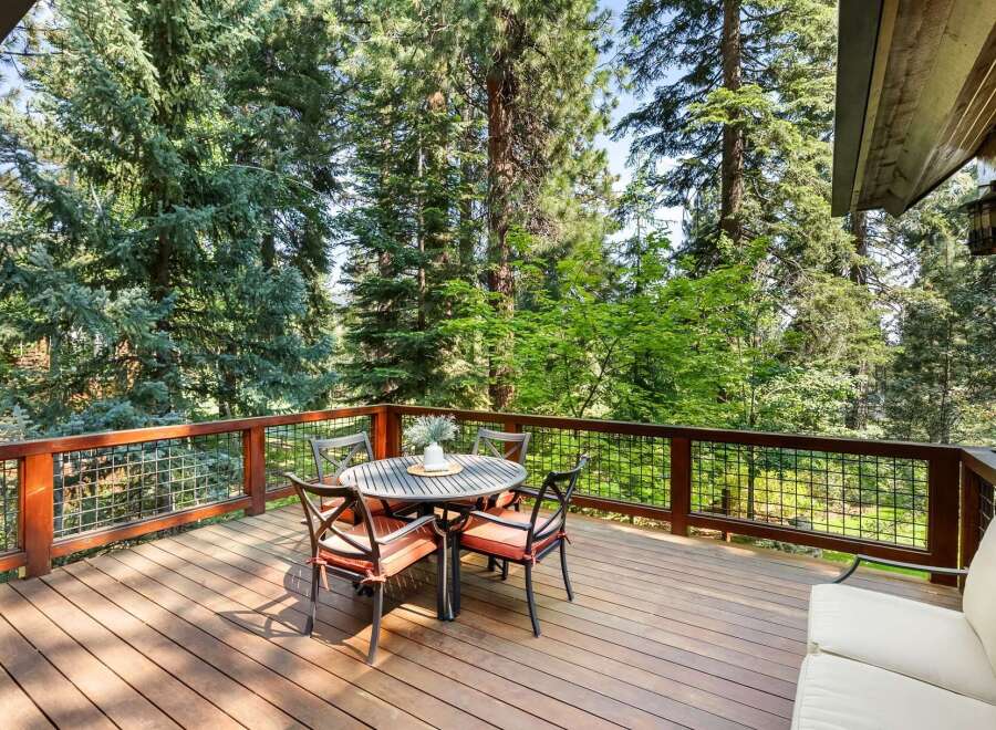 Enjoy the serene mountain lifestyle on this expansive wooden deck, perfect for outdoor dining and relaxation amidst towering trees.