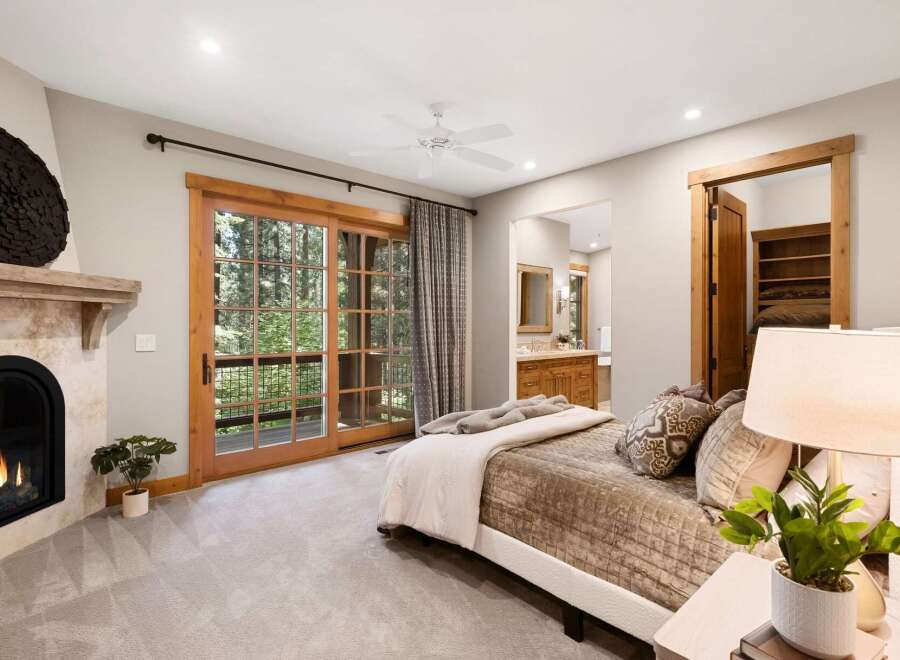 Experience luxury mountain living in this stunning bedroom featuring a cozy fireplace and expansive sliding glass doors that open to a private balcony with forest views.
