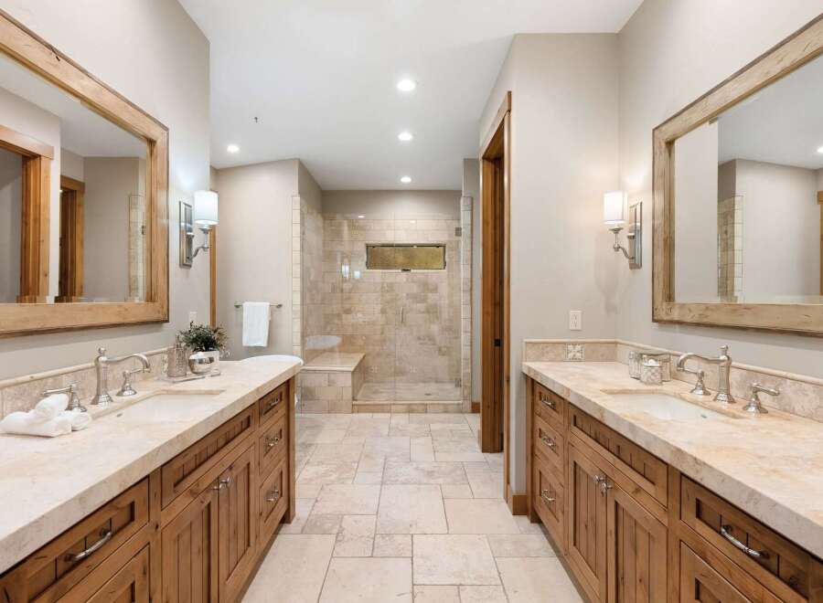 This luxurious master bathroom features dual vanities with ample counter space and custom wood cabinetry, perfect for storage.