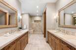 This luxurious master bathroom features dual vanities with ample counter space and custom wood cabinetry, perfect for storage.