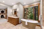 Indulge in luxury with this stunning bathroom featuring a freestanding soaking tub perfectly positioned to enjoy breathtaking forest views through a large, wood-trimmed window.