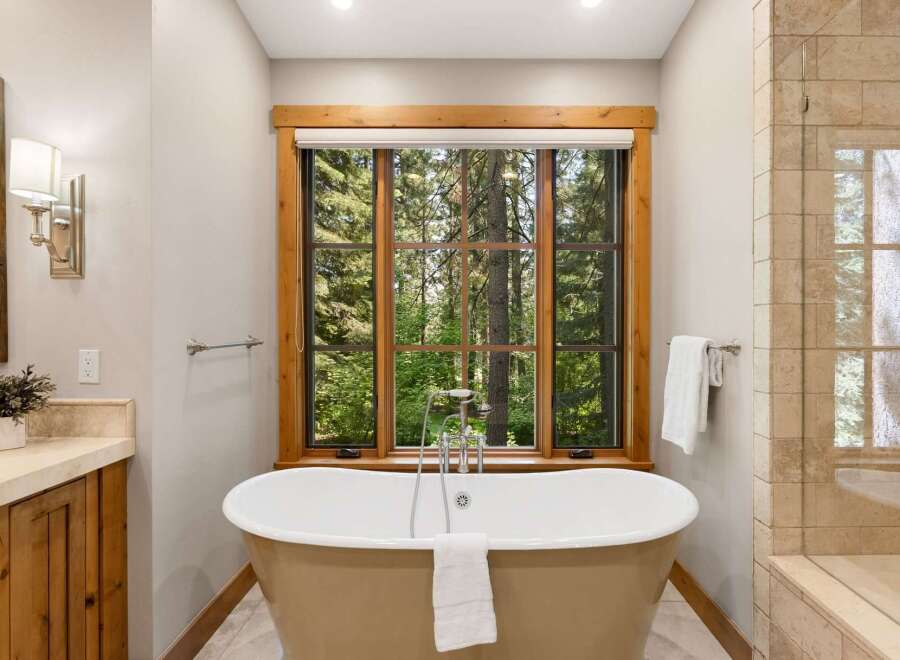 Indulge in ultimate relaxation in this luxurious bathroom, featuring a freestanding soaking tub perfectly positioned to offer serene views of the surrounding forest through a large, wood-trimmed window.