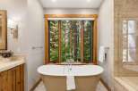 Indulge in ultimate relaxation in this luxurious bathroom, featuring a freestanding soaking tub perfectly positioned to offer serene views of the surrounding forest through a large, wood-trimmed window.